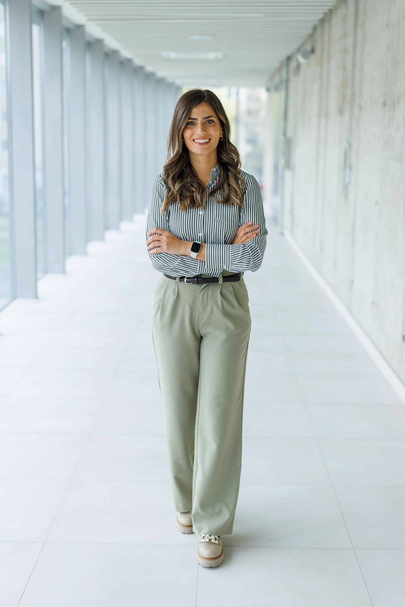 Confident young adult woman standing in modern office corridor